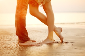 A young loving couple hugging and kissing on the beach at sunset. Two lovers, man and woman barefoot near the water. Summer in love